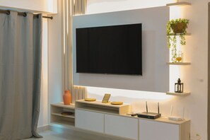 Ein modernes Wohnzimmer mit einem an der Wand befestigten Flachbildfernseher, einem weißen Konsolentisch mit Dekoration und einer Pflanze, die von der Decke hängt.