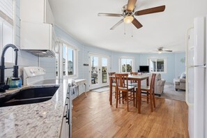 Eine moderne Küche mit einer Granit Arbeitsplatte, einem Holzes Esstisch und Stühlen. Es gibt einen Deckenventilator, einen eingebauten Backofen und einen Kühlschrank.