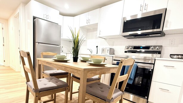 Een moderne keuken met witte kasten, een roestvrijstalen koelkast, een magnetron, een oven en een eettafel met stoelen.