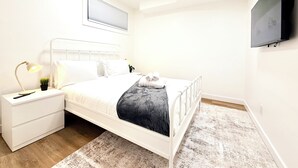 Een moderne slaapkamer met een bed, nachtkastje, lamp en een wandgemonteerde flatscreen-televisie.
