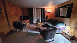 Un interior de fusta acollidor amb un sofà, butaques, una taula petita i una televisió.