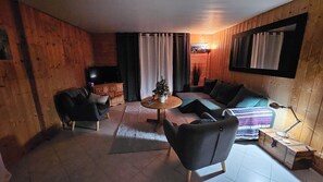 A cozy wooden interior with a sofa, armchairs, a small table, and a television. - Quiet 3-room apartment on the garden level in the mountains (Beauvezer)