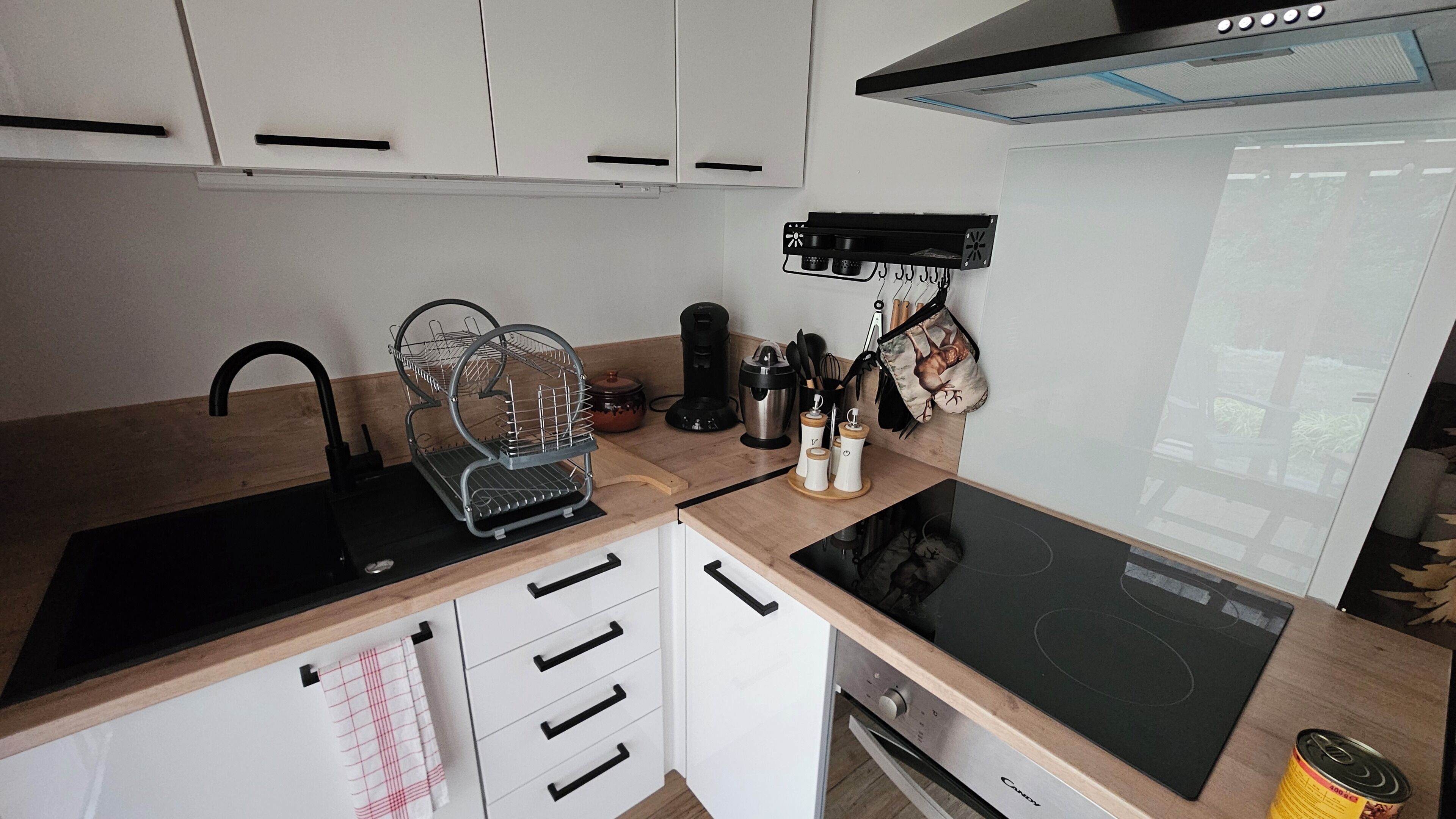 Une cuisine moderne avec des meubles blancs, une plaque de cuisson à induction noire, une machine à café et une bouilloire.