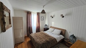 Un dormitori amb un llit de fusta, una tauleta de nit, un mirall, una finestra amb cortines i un ventilador de sostre.