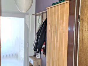 Ein Zimmer mit einem Holzschrank, einem kleinen Tisch mit Schublade und einem Kleiderhaken.