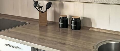 A kitchen with a wooden countertop, a stainless steel sink, and two black containers labeled 'SUGAR' and 'COFFEE'.