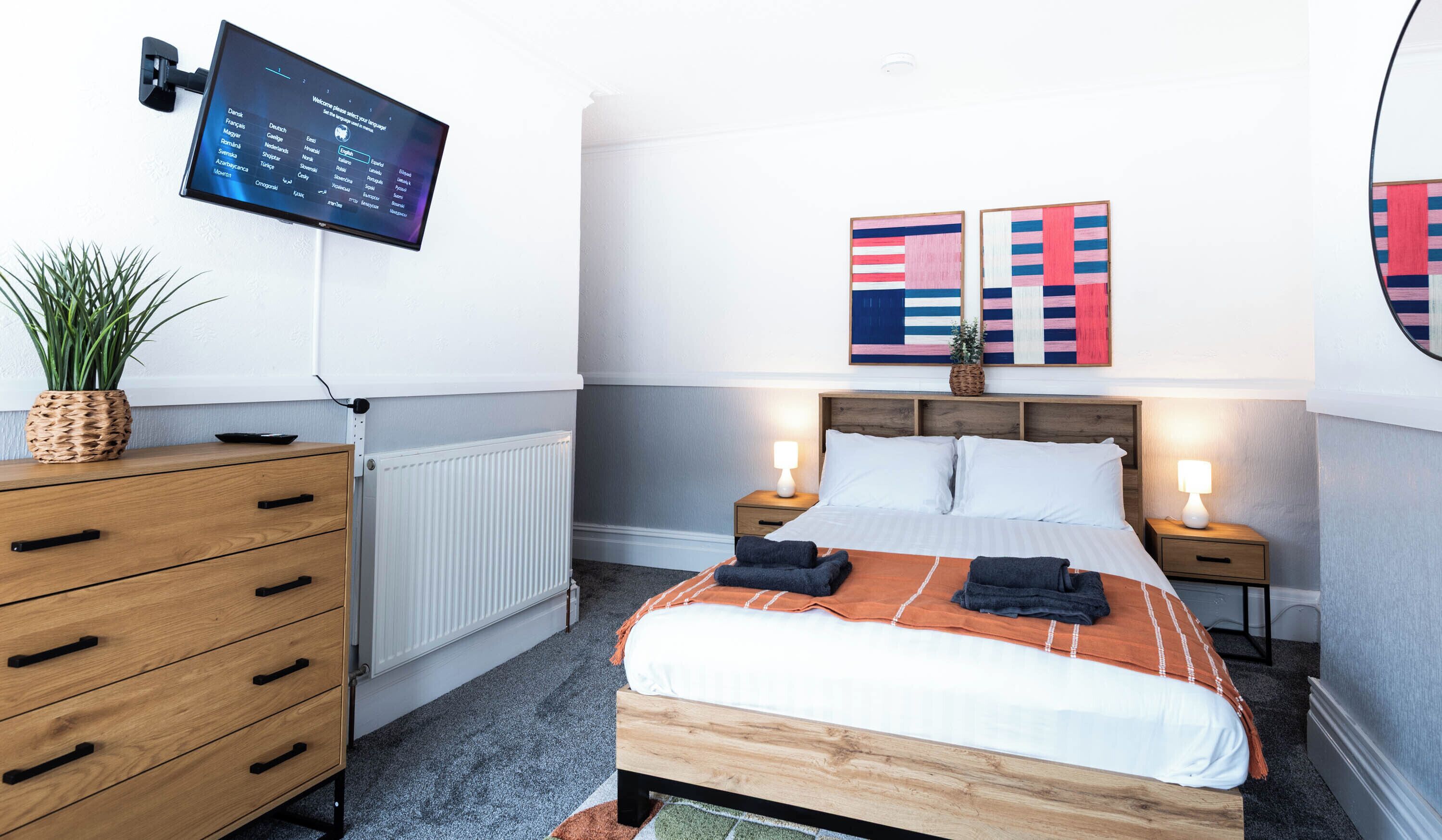 Een moderne hotelkamer met een bed, nachtkastjes, een televisie en kunst aan de muur.