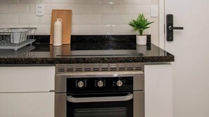 Una cocina con estufa de acero inoxidable, campana extractora blanca, una planta en maceta y una tabla de cortar de madera.