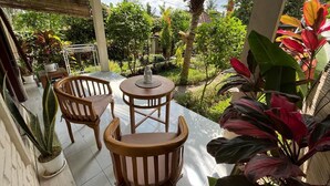 An outdoor patio with two wooden chairs and a table, surrounded by potted plants and a view of a garden. - Cozy 1-bedroom bungalow in amazing Ubud with AC (Ubud)