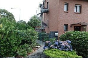A brick building with a spiral staircase leading to an upper level, surrounded by well-maintained greenery and a small garden with hydrangeas. - Bright attic studio in Cologne | Direct S11 to central station & Messe/Deutz (Köln)