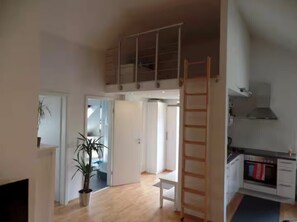 A loft-style apartment with a loft bed, a kitchen with a stove, a dining area, and a staircase. - Bright attic studio in Cologne | Direct S11 to central station & Messe/Deutz (Köln)