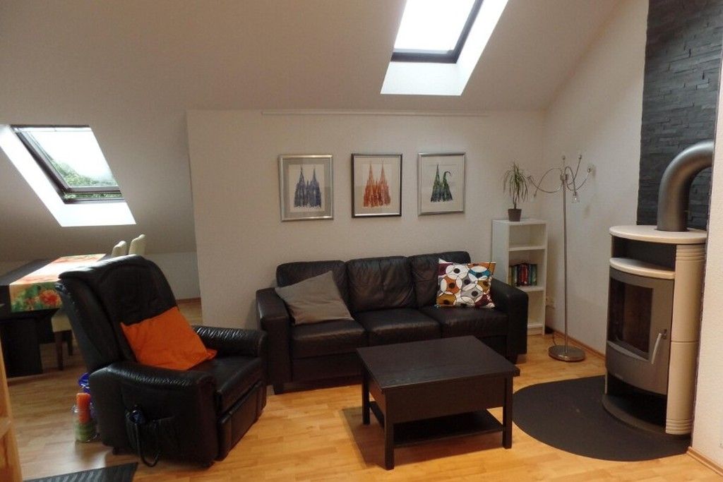 Ein Wohnzimmer mit Sofa, Sessel, Couchtisch und Kamin. Es gibt Dachfenster und gerahmte Bilder an der Wand.