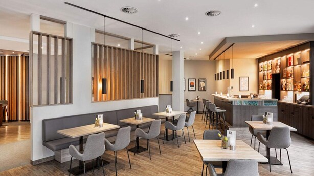 Un restaurant moderne avec des murs lambrés, plusieurs espaces de restauration et un bar proposant un large choix de boissons.