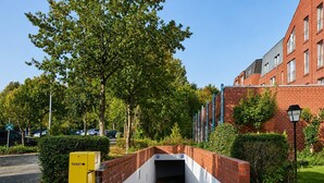 L’entrée d’un parking, avec une arche en briques, une cabine de vente de tickets jaune et, au fond, un bâtiment en briques rouges.