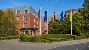 Un immeuble à plusieurs étages, doté d’une façade en briques rouges, de nombreux drapeaux et surplombé d’un ciel bleu clair.
