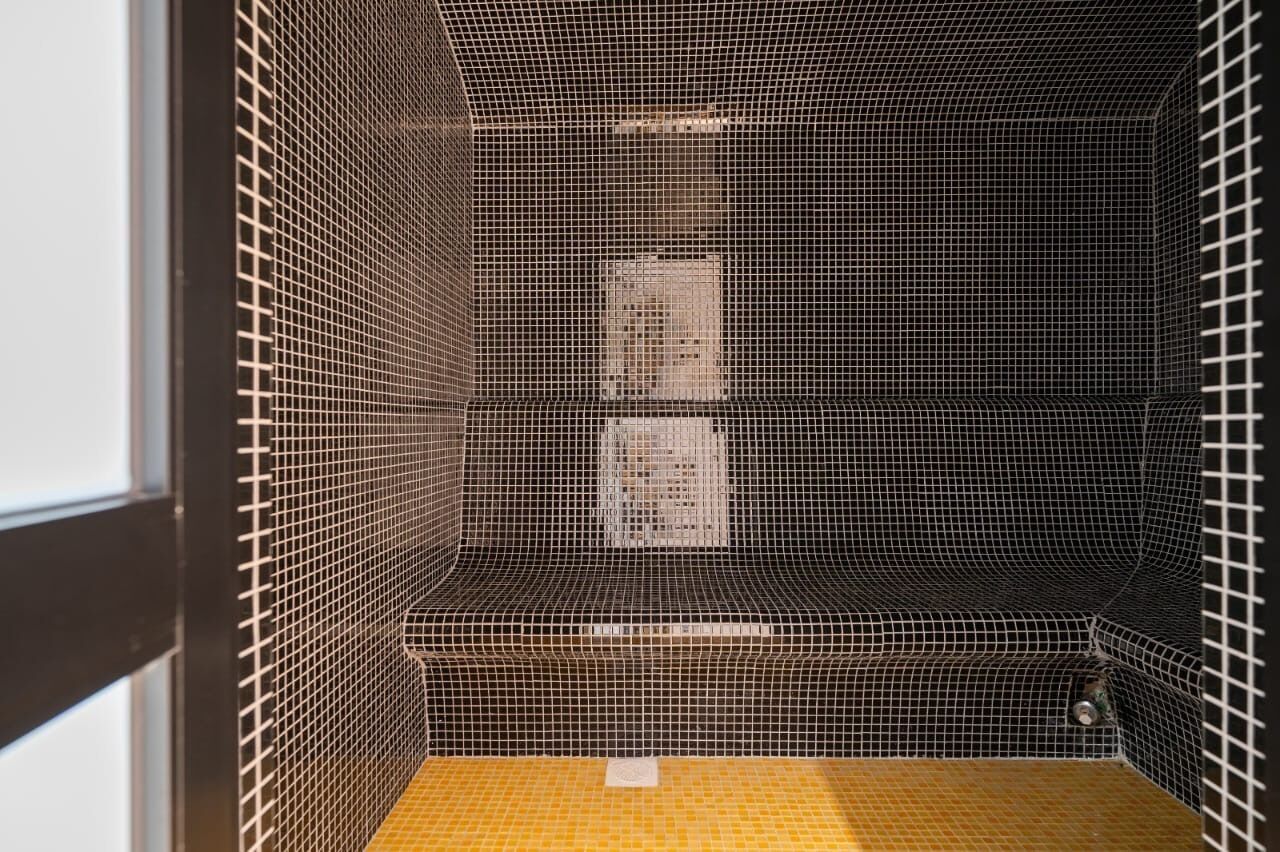 Une cabine de douche carrelée avec un sol jaune et un drain visible.