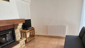 Ein Wohnzimmer mit Kamin, Fernseher auf einem Holzboden, einer Couch und einer Heizung.