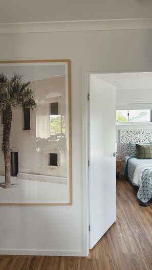Una habitació amb un llit, una porta que dona a una altra habitació i un quadre amb marc a la paret.