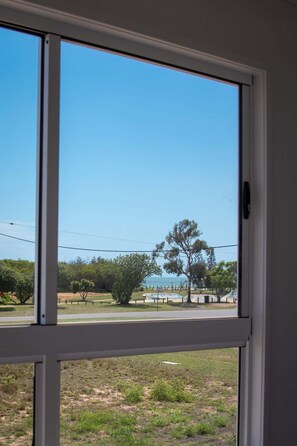 A view through a window with a clear sky, a tree, and a distant view of a park with a fence.