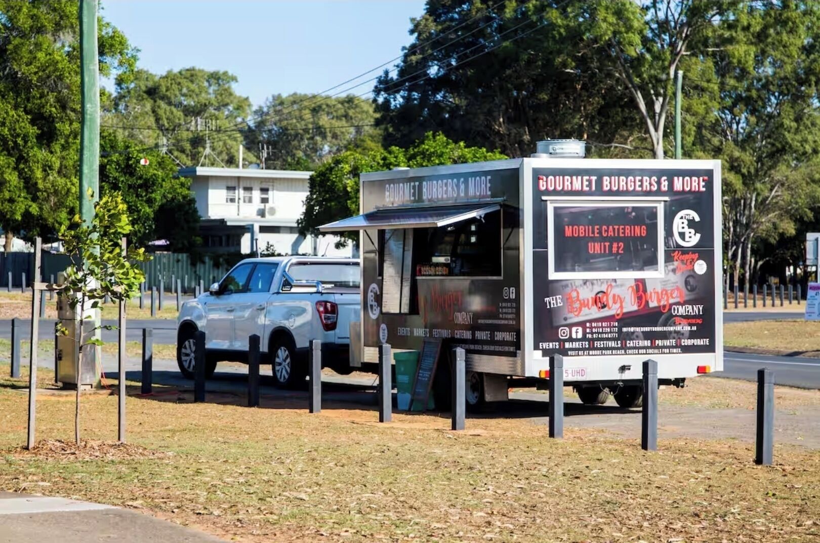A food truck with a sign advertising gourmet burgers and more, mobile catering, and The Burger Company.
