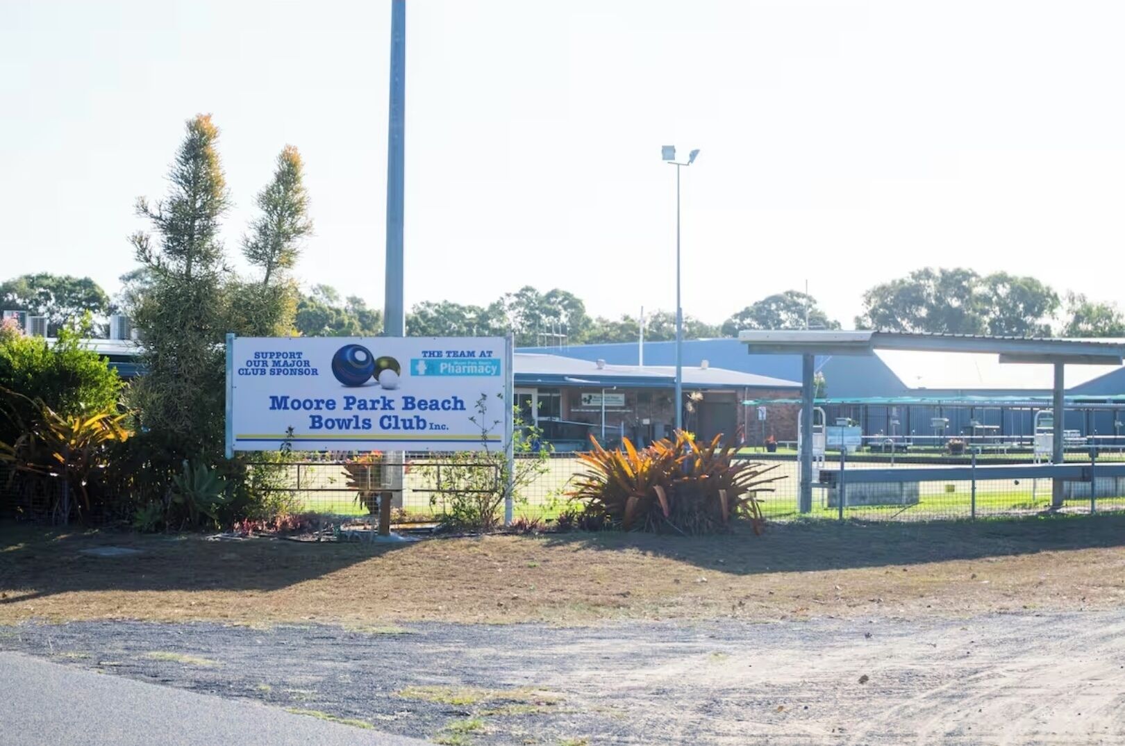 A sign for Moore Park Beach Bowls Club Inc. with a pharmacy nearby.