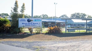 Opastekyltti, jossa näkyy Moore Park Beach Bowls Club -kerhon logo, ja lähellä on apteekki.