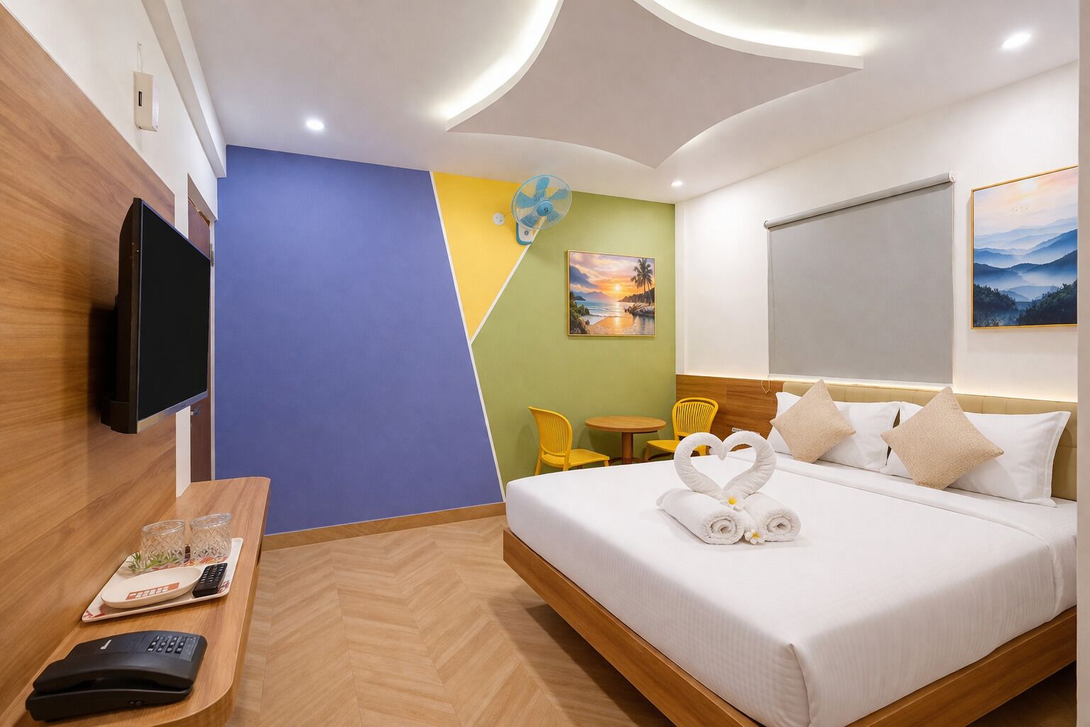 A hotel room with a bed, a TV, a desk with a remote, a chair, and a small table.