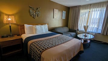 A hotel room with a bed, a desk, a chair, a small table, and a window with curtains.