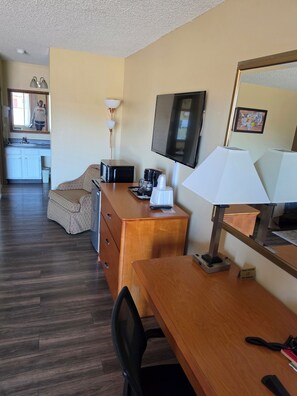 A hotel room with a wooden desk, a television, a microwave, a coffee maker, a chair, a dresser, and a small table with a lamp. - Anchor Pointe Inn & Suites (Hoquiam)