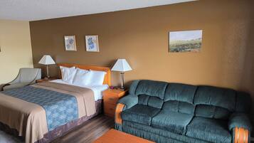 A hotel room with a bed, two bedside tables with lamps, a sofa, a wooden coffee table, and artwork on the walls.