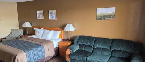 Una habitación de hotel con una cama, dos mesitas de noche con lámparas, un sofá, una mesa de centro de madera y obras de arte en las paredes.