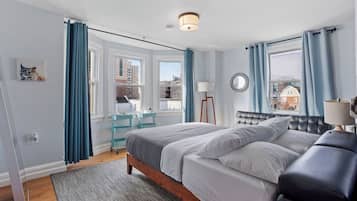 Quarto com cama, mesas de cabeceira, espelho e vista para o exterior.