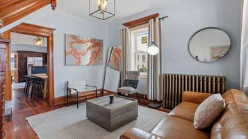 Uma sala de estar com sofá, mesa de centro e cadeiras, uma área de jantar com mesa e cadeiras, e obras de arte nas paredes.