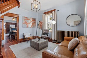Ein Wohnzimmer mit Sofa, Couchtisch und Sesseln, ein Essbereich mit Tisch und Stühlen sowie Kunstwerken an den Wänden.