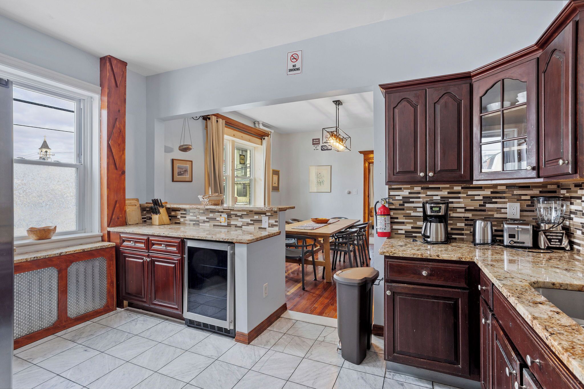Uma cozinha moderna com armários de madeira escura, bancada de granito e vista para uma sala de jantar.