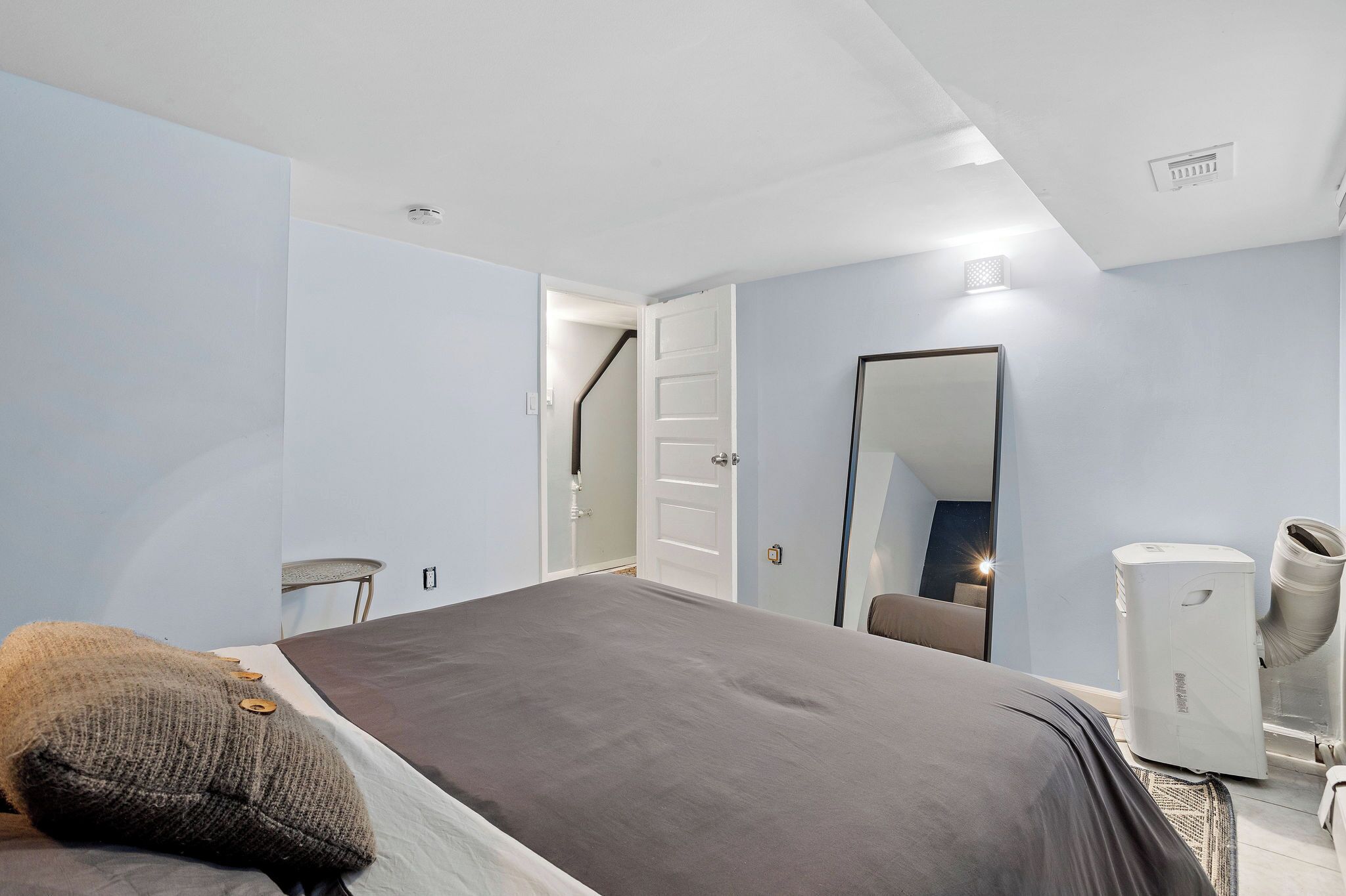 A bedroom with a bed, a mirror, a heater, and a door leading to another room.