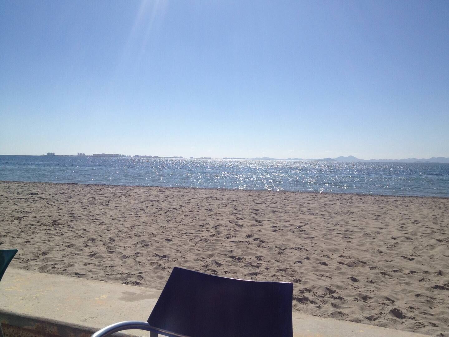 Uma praia com uma cadeira e vista desobstruída para o mar.