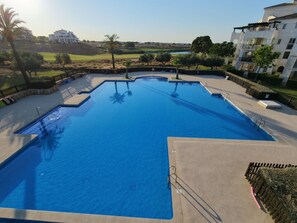 En swimmingpool med ett omgivande däck, utsikt över en golfbana och en byggnad i bakgrunden.