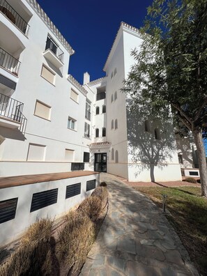 A multi-story building with balconies, a stone pathway, and a tree providing shade. - Adriatico Groundfloor Frontline Golf - 2 Bath - 3 Min Walk to Amenities (Sucina)