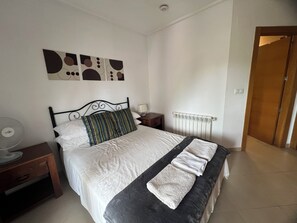 Quarto com cama, mesa de cabeceira, abajur, radiador e porta.
