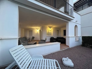 A covered outdoor seating area with a table and chairs, a white lounge chair, and a small white object on the ground. - Adriatico Groundfloor Frontline Golf - 2 Bath - 3 Min Walk to Amenities (Sucina)