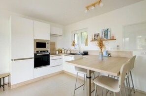 A modern kitchen with white cabinetry, a central island with chairs, a microwave, and a stove. - Apartment Near the Beaches - Sleeps 6 - Théoule-sur-Mer (Théoule-sur-Mer)