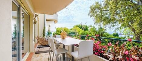 An outdoor patio with a table and chairs, a pergola, and a view of greenery and a body of water.