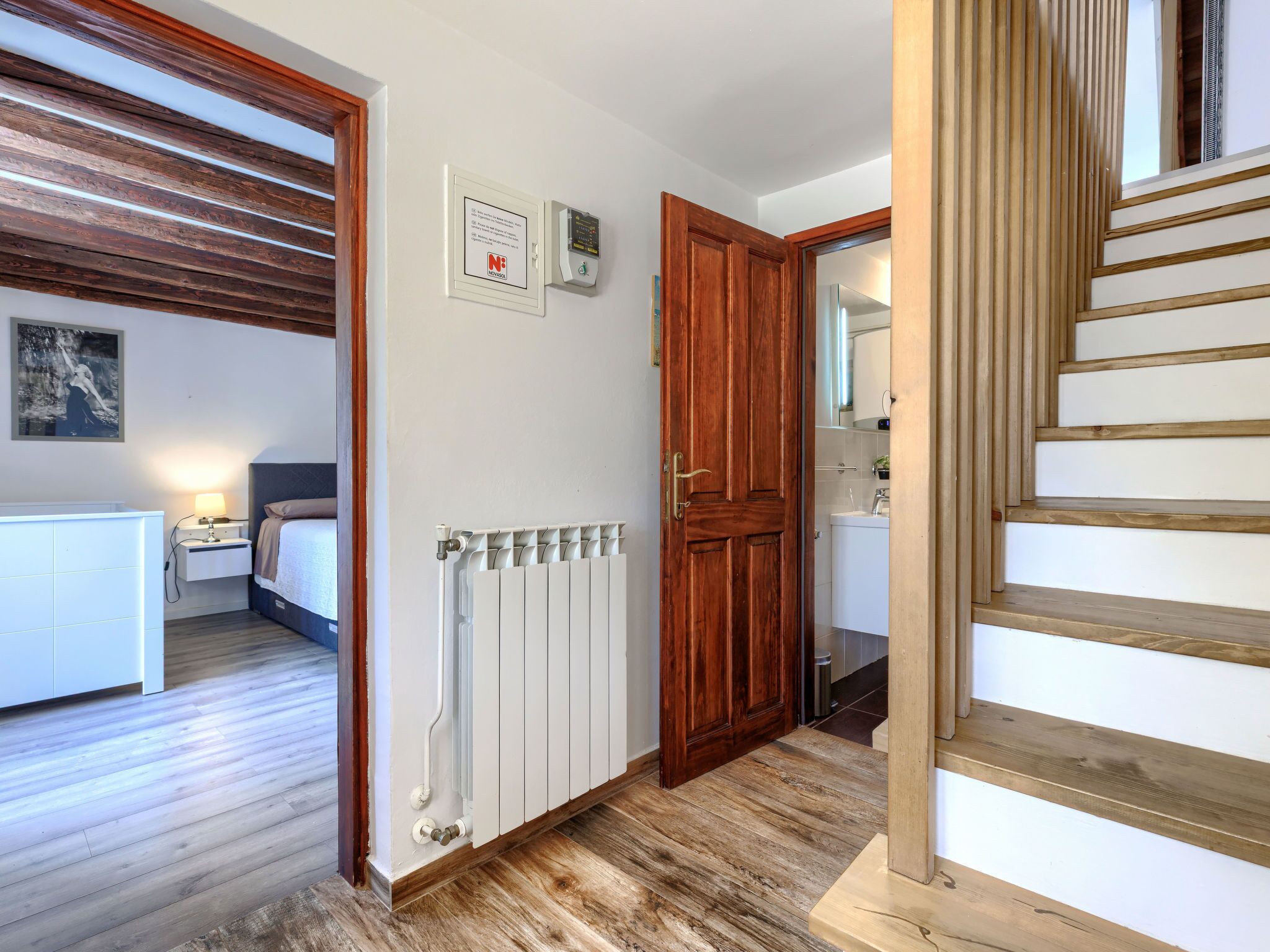 Een hotelkamer met een houten vloer, een witte radiator, een houten deur en een trap.