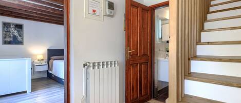 Une chambre d’hôtel avec un plancher en bois, un radiateur blanc, une porte en bois et un escalier.