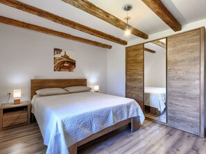 Een slaapkamer met een houten bed, nachtlampjes, een nachtkastje, een houten garderobe en een schilderij van de Eiffeltoren.