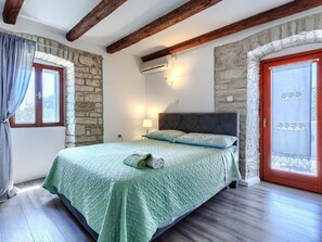 Ein Schlafzimmer mit Bett, Steinwänden, Holzbalken, einem Fenster und einer Klimaanlage.
