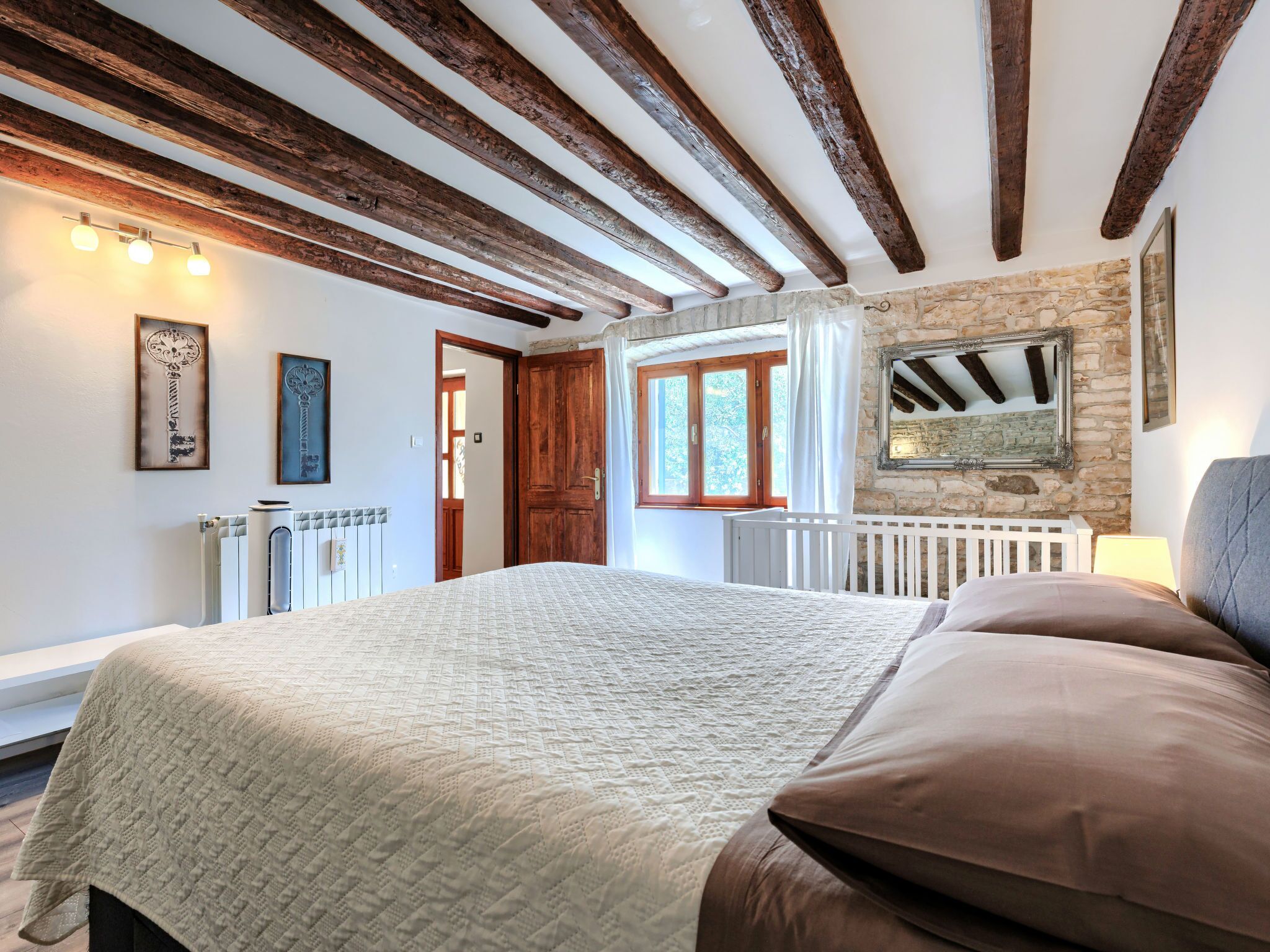 Ein Schlafzimmer mit einem großen Bett, Holzbalken, einer Steinwand und einem Fenster.