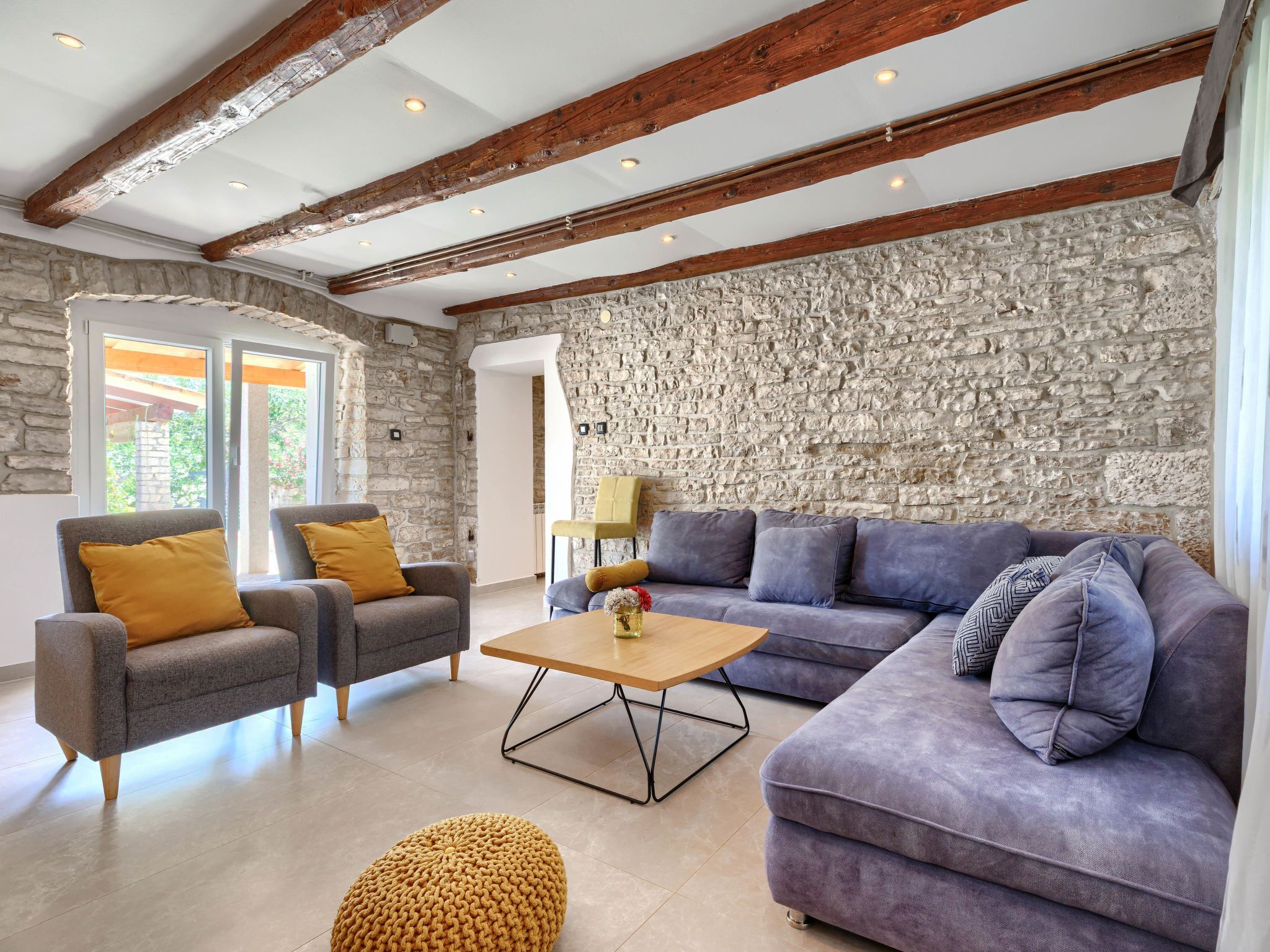 Ein Wohnzimmer mit Steinwänden, Holzbalken, einem Sofa, Sesseln und einem Couchtisch.