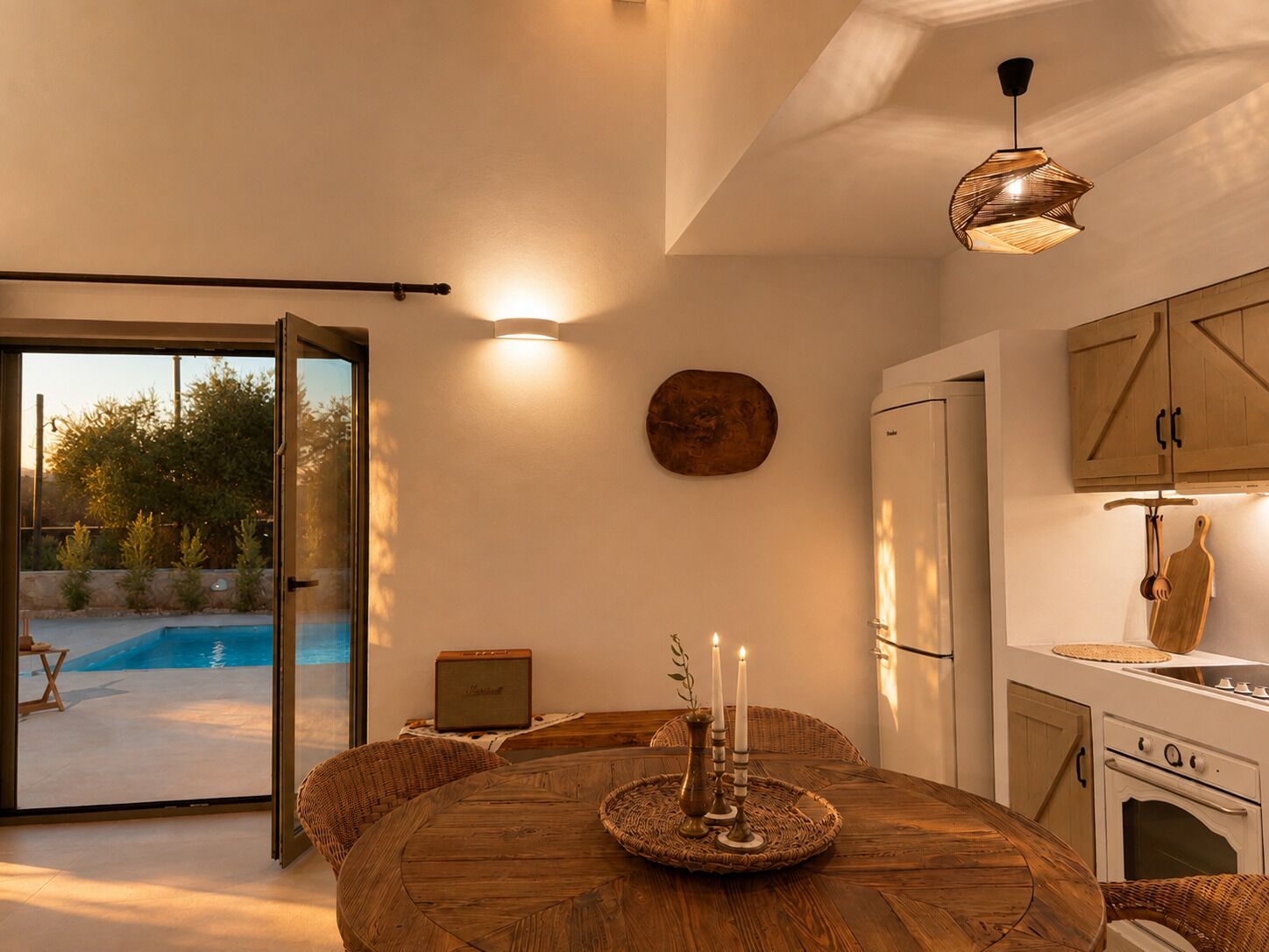 Una cucina moderna con un tavolo rotondo in legno, piano cottura integrato e vista su una piscina attraverso porte in vetro.